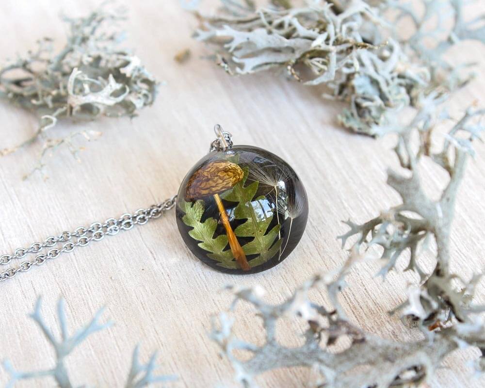 Pendant necklace with autumn elements inside resin: golden mushroom cap, green fern and dandelion seed, surrounded by pale lichen
