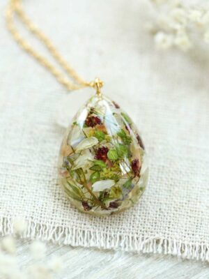 Flat-lay view of a botanical resin necklace with mixed dried flowers on a light fabric surface.