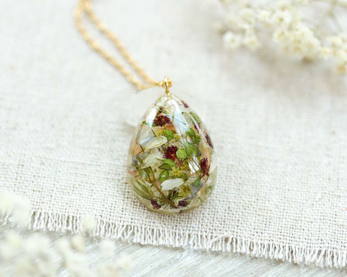 Flat-lay view of a botanical resin necklace with mixed dried flowers on a light fabric surface.