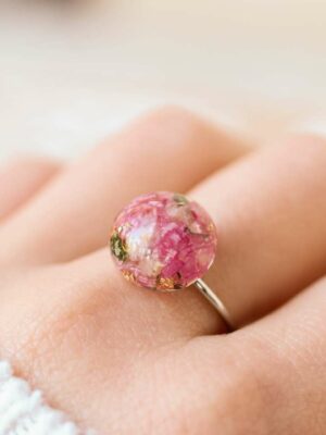 Close-up of a handcrafted resin ring worn on a finger, featuring vibrant pink floral elements preserved from a bridal bouquet.