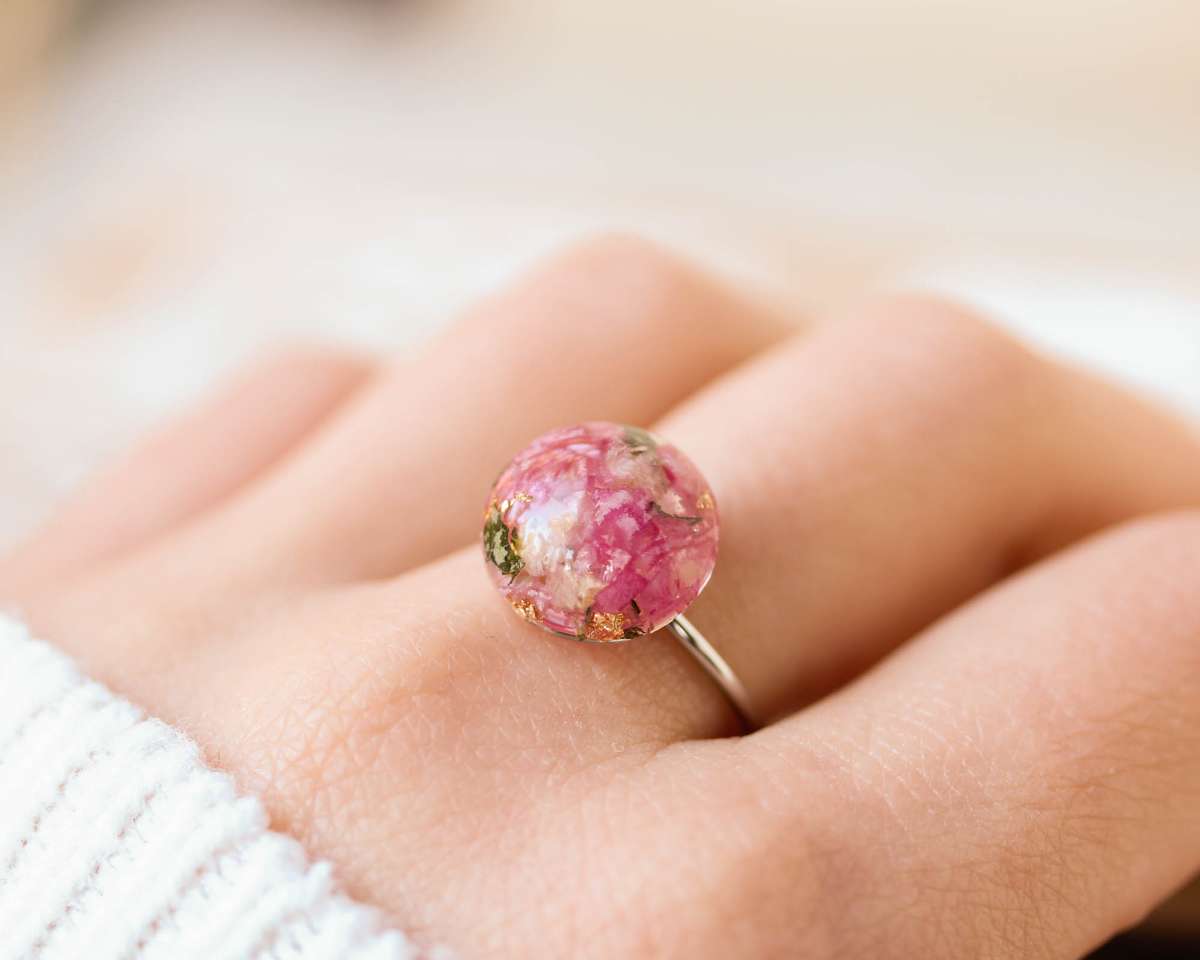 Close-up of a handcrafted resin ring worn on a finger, featuring vibrant pink floral elements preserved from a bridal bouquet.