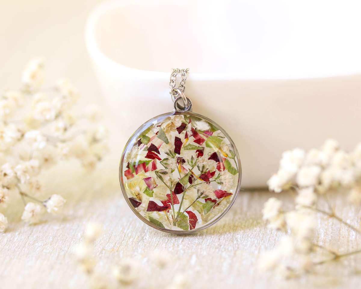 Circular resin pendant necklace with preserved funeral flowers in red, white, and green tones.