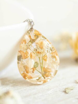 Handmade teardrop necklace with dried neutral-toned flowers, leaning against a white bowl.
