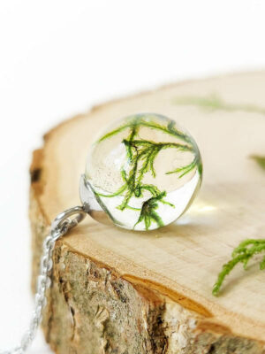 Resin necklace with preserved moss styled flat on a round wooden base, surrounded by delicate lichen accents