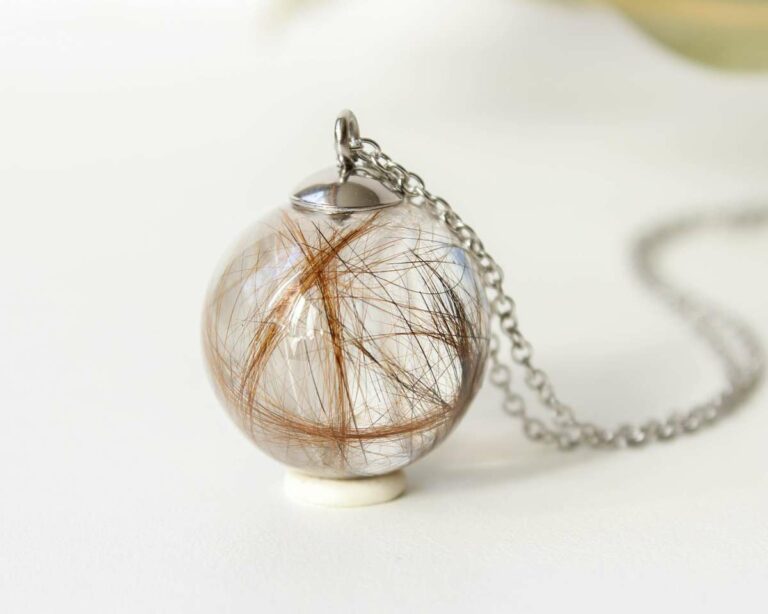 Close-up of a pet hair memorial pendant in a clear resin sphere with silver chain.