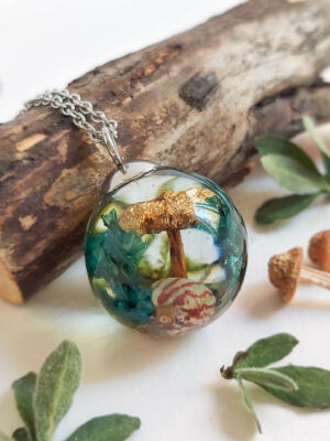 Nature-inspired resin pendant featuring a brown mushroom, preserved greenery, and a pink-and-cream striped shell, placed beside twigs and leaves.