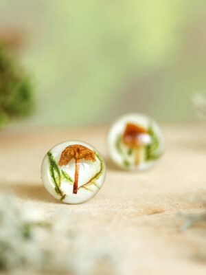 Close-up of mushroom resin earring in focus with soft forest background.