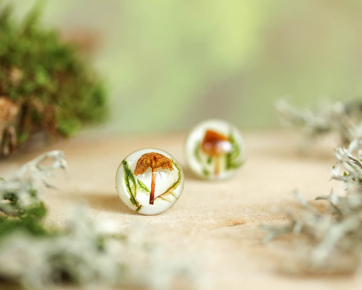Close-up of mushroom resin earring in focus with soft forest background.