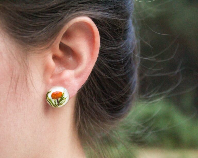 Handmade mushroom earrings held in hand for size reference.