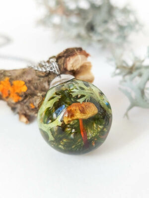 Artisan resin necklace with a real forest mushroom, moss, and lichen, placed on a white surface with soft light