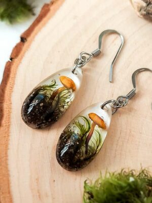 Flat lay of mushroom and moss teardrop earrings on a wooden slice.