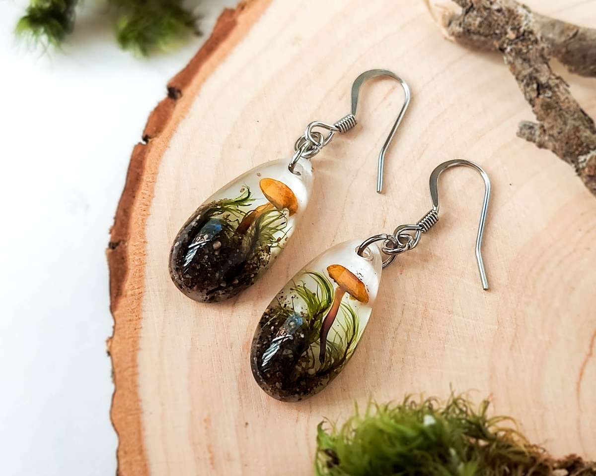 Flat lay of mushroom and moss teardrop earrings on a wooden slice.