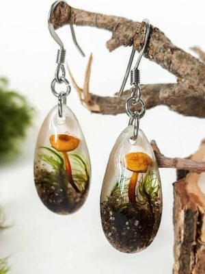 Nature-inspired resin earrings with mushrooms and moss, hanging from a tree branch.