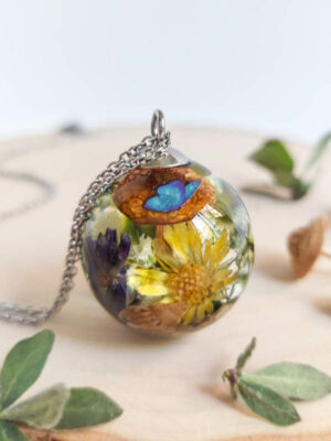 Pendant on wooden surface showcasing a vivid arrangement of yellow petals, mushroom, and butterfly wing inside resin.