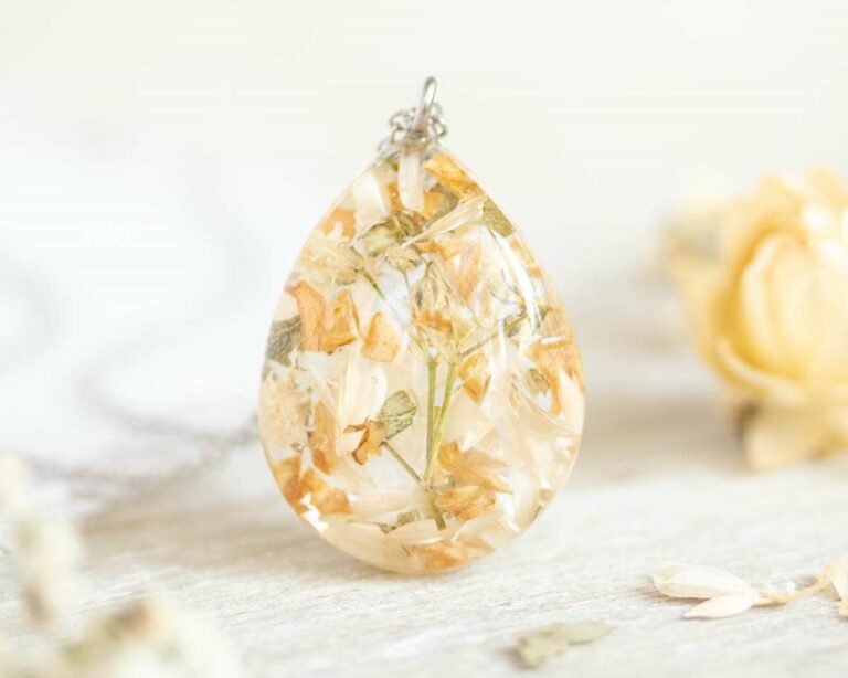 Standing teardrop resin pendant with delicate beige and white dried flowers arranged inside.