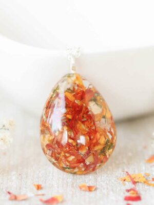 Wedding flower resin pendant necklace displayed against a white ceramic bowl, surrounded by white baby’s breath flowers.