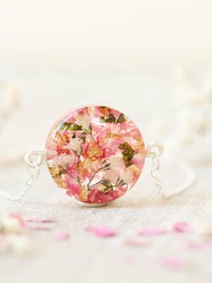 Macro shot of a round keepsake bracelet in translucent resin, highlighting embedded dried wedding flowers and gold accents, surrounded by soft white blooms.