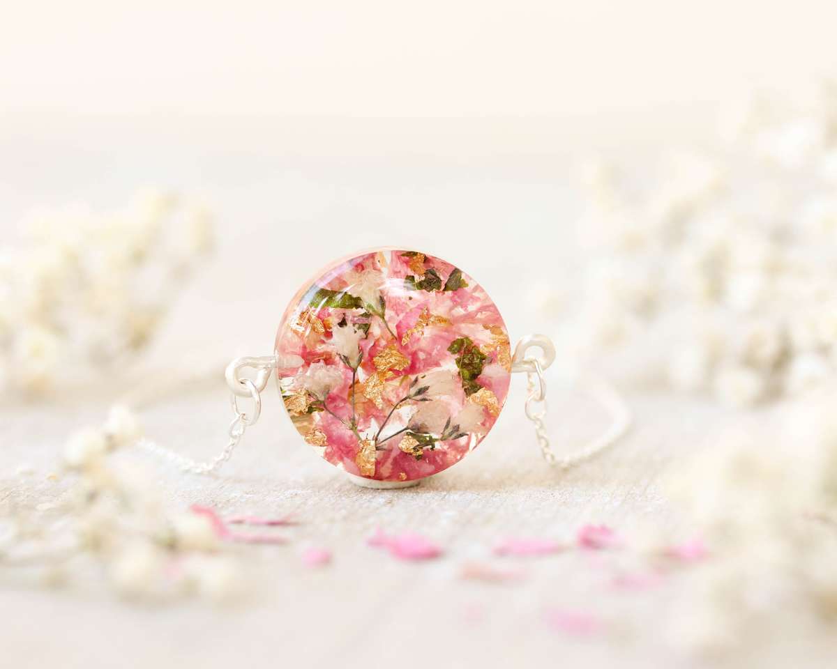 Macro shot of a round keepsake bracelet in translucent resin, highlighting embedded dried wedding flowers and gold accents, surrounded by soft white blooms.