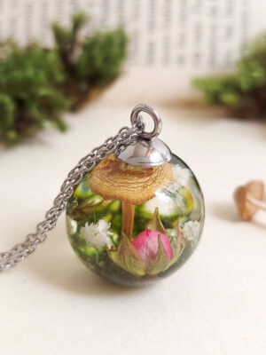 A spherical pendant with a real mushroom and pink flower encased in resin, evoking the feeling of a hidden woodland corner.