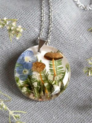 Front view of the round pendant with mushrooms, white and blue flowers, and ferns inside resin