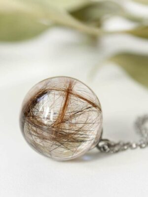 Resin sphere pendant with brown and black pet hair inside, laid on a white background.