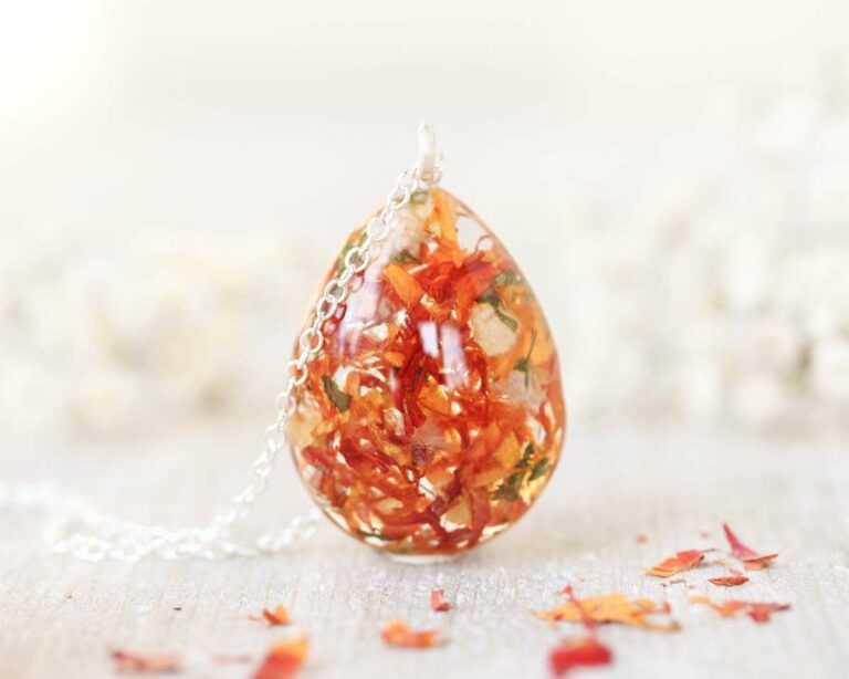 Close-up of a vibrant orange floral teardrop pendant with visible flower textures and a silver chain.