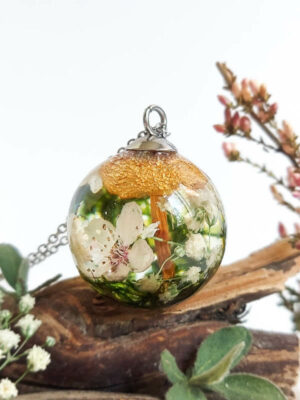 Resin necklace with cherry blossom, moss, and mushroom displayed on wood and surrounded by small flowers