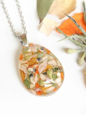 Custom resin necklace displayed flat with vibrant dried wedding flowers in orange, gold, and soft pink tones.
