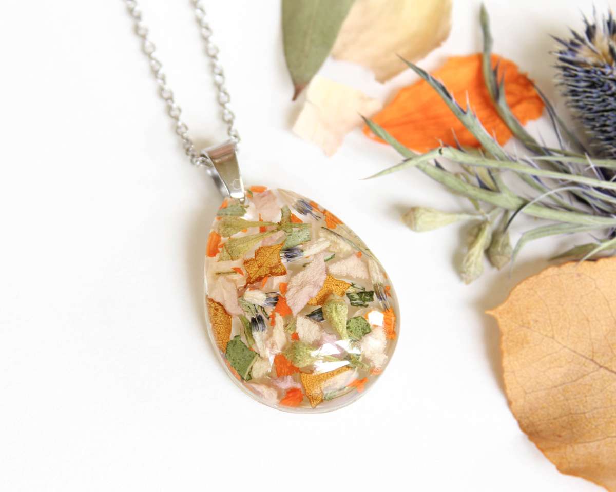 Custom resin necklace displayed flat with vibrant dried wedding flowers in orange, gold, and soft pink tones.