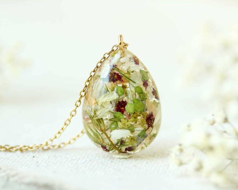 Teardrop-shaped resin pendant with preserved red, green, and white flowers, hanging from a gold chain.