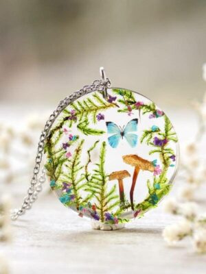 Bright and vibrant necklace with a central blue butterfly, mushrooms, and lush green ferns, set in a clear resin circle with a silver chain.