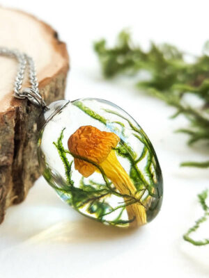 Close-up view of a transparent resin pendant showcasing a real mushroom and forest greenery