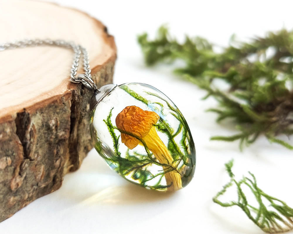 Close-up view of a transparent resin pendant showcasing a real mushroom and forest greenery