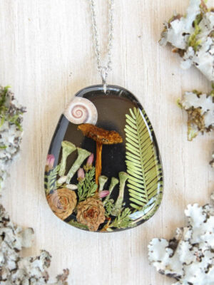 Handmade forest necklace placed on textured bark with detailed miniature elements