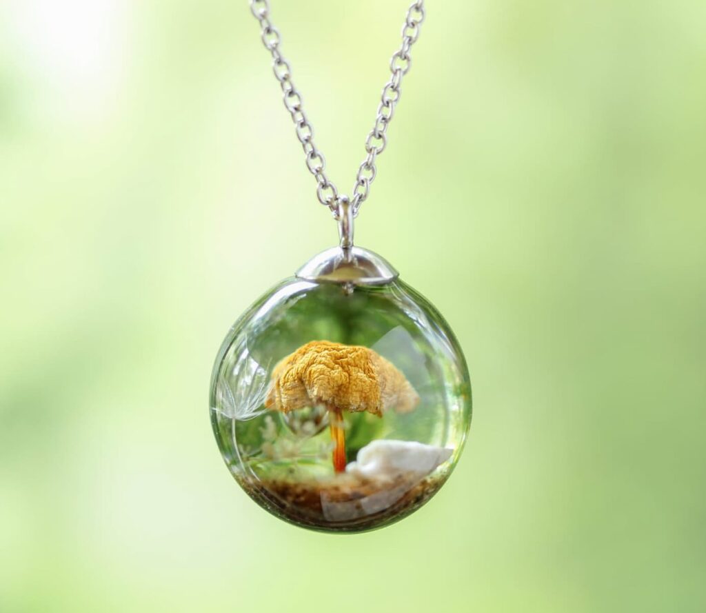 Handmade resin pendant by Botania Jewelry featuring a preserved real mushroom, dandelion seed, and forest details inside